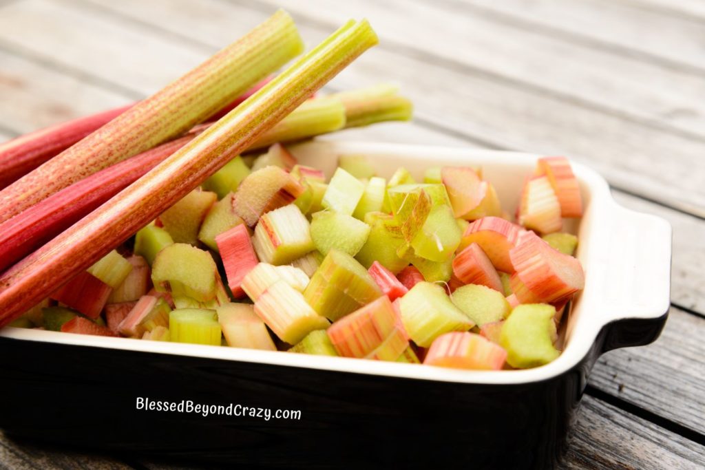 Stalks of fresh rhubarb and small baking dish with cut rhubarb.