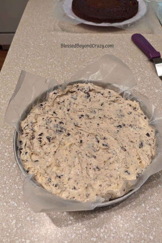 Frozen Oreo ice cream pressed into round cake pan with chocolate cake layer in the background.